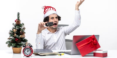 holiday festive mood with young tired angry business person with santa claus hat holding his bank card office white background
